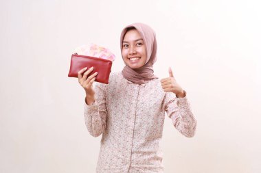 Excited young asian muslim girl standing showing thumbs up while holding Indonesian banknotes on her wallet
