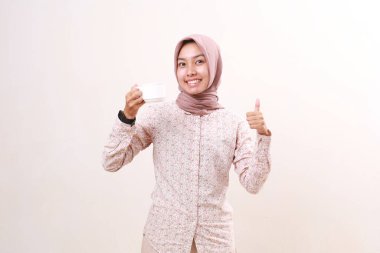 Happy young asian muslim girl holding a cup of drink while showing thumbs up. Isolated on white