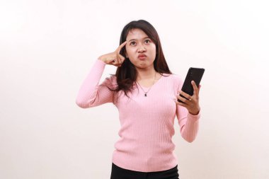 Confused young asian girl holding a cell phone while thinking an idea. Isolated on white background