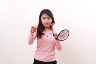 Confused angry young asian girl standing holding megaphone while pointing at the camera. Isolated on white background