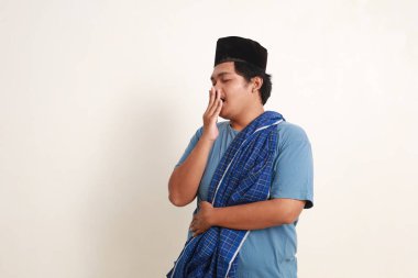 Uykulu Asyalı genç Müslüman çocuk, kep ve kınalı esneme sırasında ayakta duruyor.