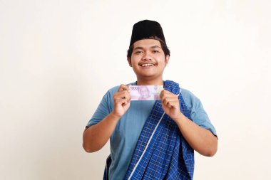 Mutlu Asyalı Müslüman çocuk ayakta dururken nakit on bin rupiah gösteriyor.