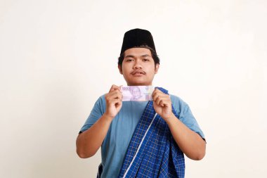 Üzgün Asyalı Müslüman çocuk ayakta dururken 10 bin rupiah nakit para gösteriyor.