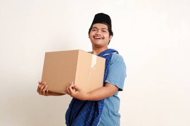 Mutlu gülümseyen Asyalı Müslüman çocuk elinde bir paketle ayakta duruyor.