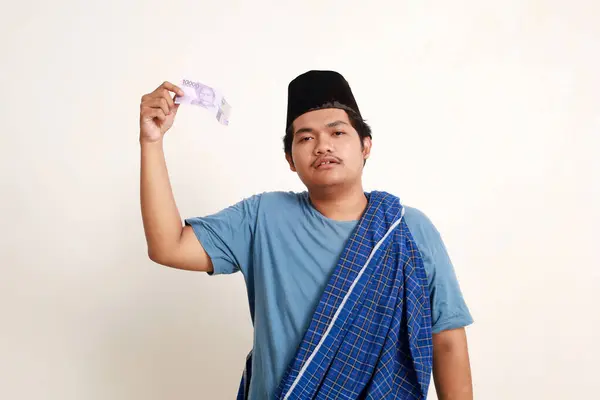 Sad asian muslim boy standing while showing ten thousand rupiah in cash