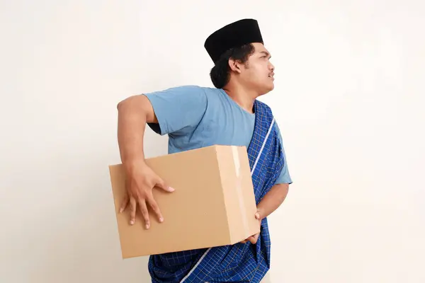 Side view of asian muslim boy standing carrying a heavy package