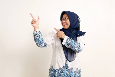 Mutlu Asyalı yaşlı Müslüman kadın boş uzayı işaret ediyor ve yan bakıyor. Beyazda izole edilmiş