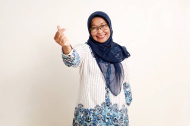 Asyalı yaşlı Müslüman kadın mutlu bir ifadeyle sevgi dolu kalp şeklinde bir jest gösteriyor.