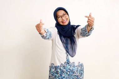 Asyalı yaşlı Müslüman kadın mutlu bir ifadeyle sevgi dolu kalp şeklinde bir jest gösteriyor.