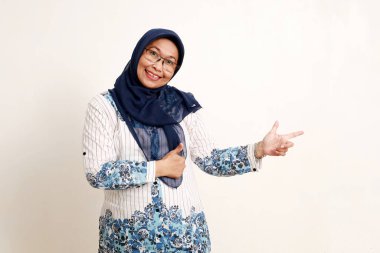 Mutlu Asyalı yaşlı Müslüman kadın yan tarafı göstererek el hareketi yapıyor.