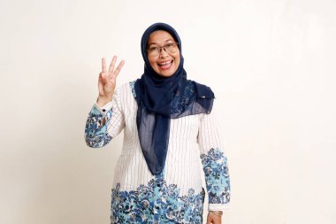 Asyalı Müslüman kadın üç parmağını göstererek ayakta duruyor.