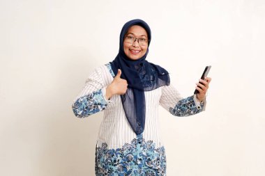 Asyalı yaşlı Müslüman kadın baş parmağını kaldırırken elinde cep telefonu tutuyor.