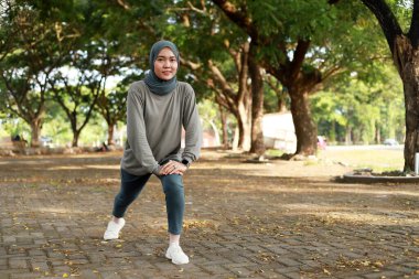 Peçeli Asyalı kız parkta egzersiz yapmadan önce ayağını uzatıyor.