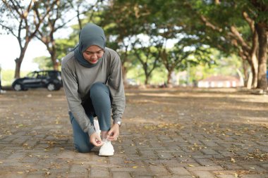 Spor kıyafetleri içinde Müslüman bir kadın parkta egzersiz yaparken ayakkabı bağcıklarını düzeltiyor.