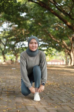 Spor kıyafetleri içinde Müslüman bir kadın parkta egzersiz yaparken ayakkabı bağcıklarını düzeltiyor.