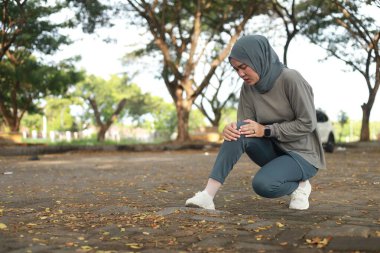Eklem ağrısı, eklem iltihabı ve tendon sorunları. Asyalı Müslüman bir kadın parkta dizine dokunuyor.