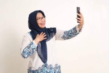 Mutlu Asyalı yaşlı Müslüman kadın selfie çekerken ya da video çekerken ayakta duruyor.