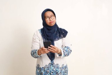 Düşünceli Asyalı yaşlı kadın elinde cep telefonuyla gökyüzüne bakıyor.