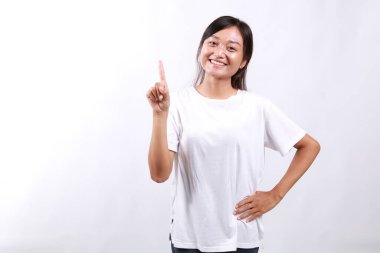 Gülümseyen, güzel görünümlü Asyalı bir kız tavsiye veriyor, bir parmağını açık olarak gösteriyor, işaret ediyor, beyaz arka planda duruyor.