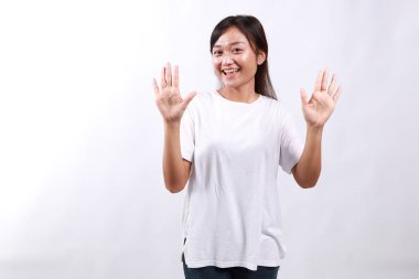 Gülümseyen mutlu Asyalı kız tavsiye veriyor, on parmağını gösteriyor kuralları açıklarken, işaret ediyor, beyaz arka planda duruyor.
