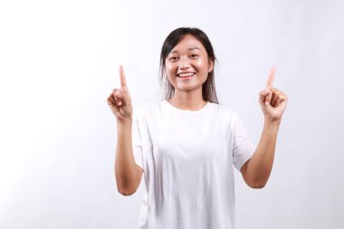 Neşeli genç Asyalı kadın yeni ürün paylaşımı tanıtımını sizlerle yapıyor, parmaklarınızı kaldırıp gülümsüyor, heyecanlı ve neşeli görünüyor, hevesli reklamlar yapıyor, beyaz arka planda duruyor.