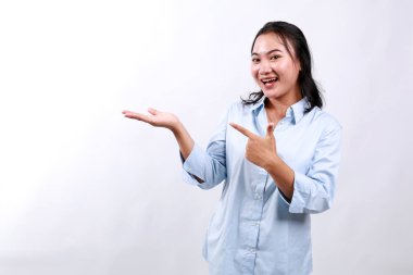 Gülümseyen sevimli Asyalı kadın duyuru yapıyor, yeni ürünü tanıtıyor, reklamınız için boş bir yeri işaret ediyor, beyaz arka planda duruyor.