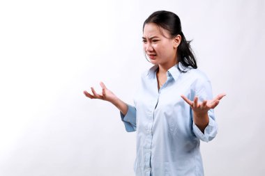 Kafası karışmış Asyalı kız elleri boş ve yana bakıyor, omuzlarını silkiyor, beyaz arka planda duruyor.