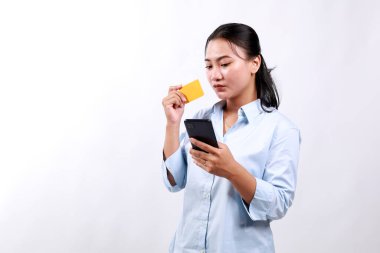 Asyalı kurumsal kadın düşünüyor, elinde akıllı telefon ve kredi kartı tutuyor, internetten smth almayı planlıyor, cep telefonuyla alışveriş yapıyor, beyaz arka plan