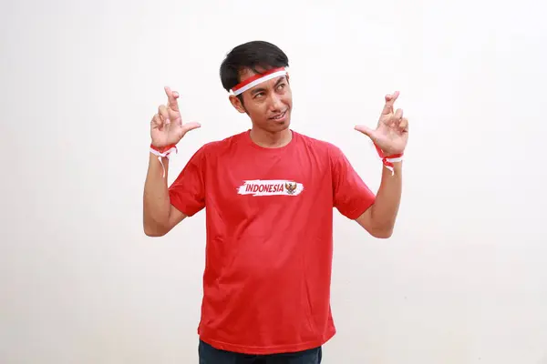 stock image Young asian boy with red white ribbon celebrating Indonesia independence day while making cross fingers, hope gesture