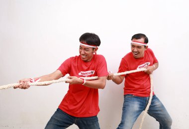 Two Indonesian men celebrate Indonesian independence day on 17 August with the tug of war contest isolated over white background