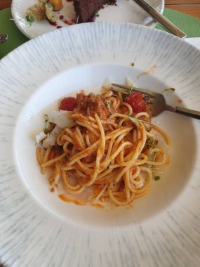 Domates soslu spagetti ve kırmızı biber ve ahşap mutfakta beyaz bir tabak.