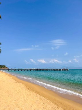 Tahta iskelesi ve turkuaz suları olan güneşli sahil.