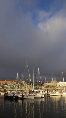 Bir limanda yelkenliler dramatik bir gökyüzü altında Güneş Işığının Suyun Üzerinde Yansıması