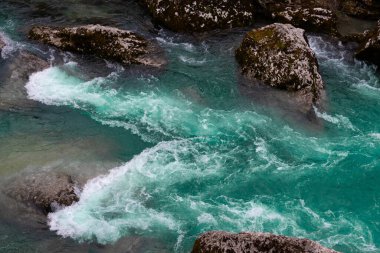 Kristal berraklığında turkuaz su kayaların üzerinden akıyor, dinamik ve güçlü bir nehir manzarası yaratıyor..