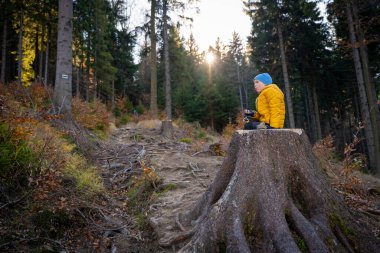 Küçük çocuk dağ yolunda büyük bir kütüğün üzerinde oturmuş yemek yiyor. Sonbahar sezonu