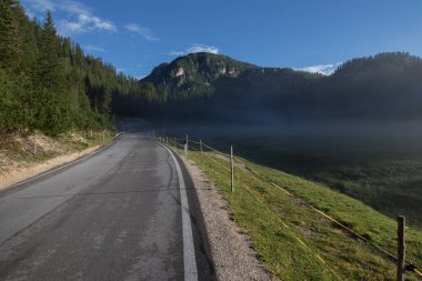 Küçük, hafif bir sabah sisi asfalt yolda çayırın üzerinde yükseliyor. Dolomite, İtalya.