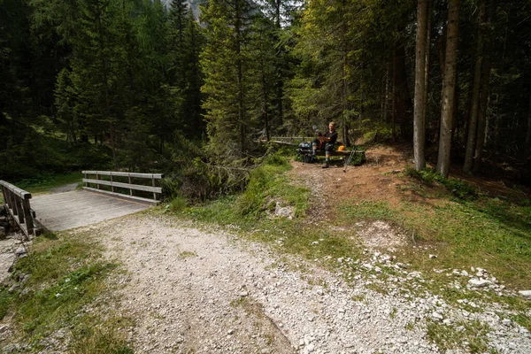 A tourist on a bench by the trail cleans shoes. Dolomites, Italy