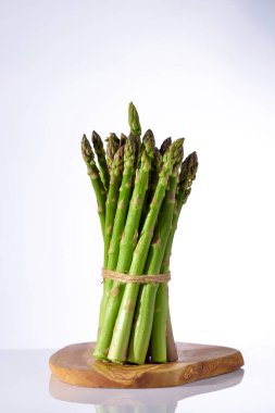 Beyaz arka planda ahşap tabakta yeşil kuşkonmaz