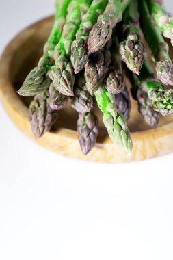 Beyaz arka planda ahşap tabakta yeşil kuşkonmaz