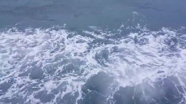 Okyanus dalgalarının yakın çekim görüntüsü su yüzeyinde beyaz köpük oluşturuyor..