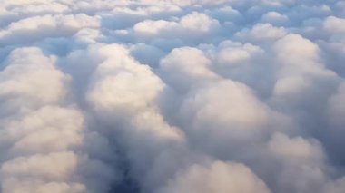 Parlak mavi gökyüzünün altında uçağın kanadının ve kabarık bulutların manzarası..