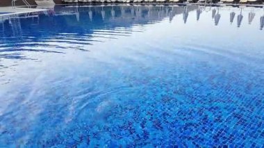 Parlayan mavi bir yüzme havuzunun huzur dolu bir görüntüsü. Işıkların yansımalarıyla aydınlatılmış..