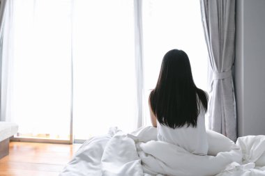 Güzel Asyalı kadın modern yatak odasında uyandıktan sonra yatakta dinleniyor.