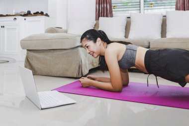 Evde sağlıklı egzersiz konsepti, Asyalı fit kadın dizüstü bilgisayarla evde kalıp spor antrenmanı, covid-19 salgınının yeni normal hayatı.