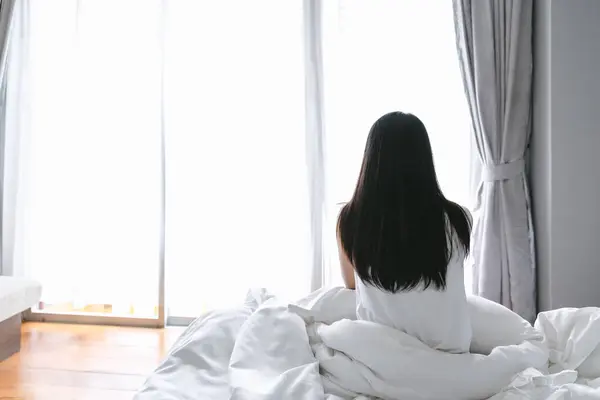 美しいアジアの女性は モダンなベッドルームで目覚めた後 ベッドでリラックス ロイヤリティフリーのストック写真