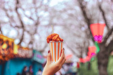 Tokyo, Japonya 'da kiraz çiçeği festivali geçmişi olan Asyalı bir kadının elinde karaage kızarmış tavuk aperatifi, Japon sokak yemekleri kavramı.