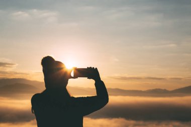Kış tatili konsepti, kazak ve yün şapkalı Asyalı genç gezgin kadın fotoğraf çekiyor ve cep telefonuyla Tayland, Mae Hong Son 'da gün doğumunda sisle dağda selfie çekiyor.