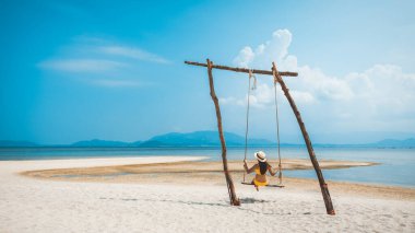 Yaz tatili konsepti, bikinili ve şapkalı mutlu Asyalı kadın Koh Rap, Samui, Surat Thani, Tayland 'da salıncakta sallanıyor.