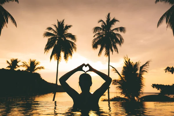 夏の旅行の休暇のコンセプト シルエット幸せな旅行者アジアの女性はリラックスし タイのコオドの日没でビーチの背景でリゾートで無限のプールでハートの形を作る ストック写真