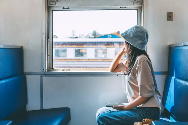 旅行輸送コンセプト 携帯電話でハッピー旅行アジアの女性はリラックスして窓の近くに座って 地元の列車で眺めている ロイヤリティフリーのストック画像